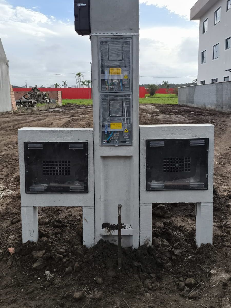 Poste padrão com duas caixas entre duas muretas, em terreno em obra